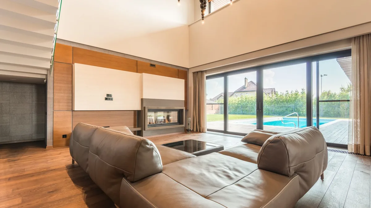 Salón moderno con un sofá de piel y una gran puerta corredera de cristal abierta hacia una piscina exterior.