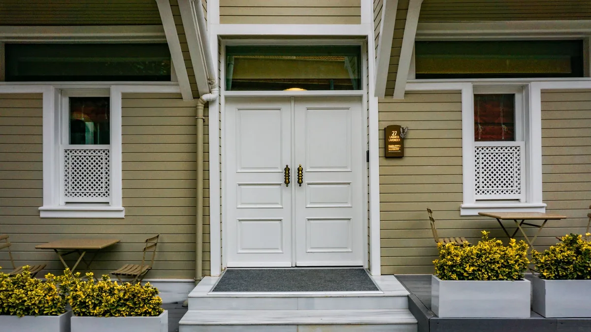 Entrada de una vivienda con una puerta doble blanca de paneles y tiradores decorativos, flanqueada por macetas.