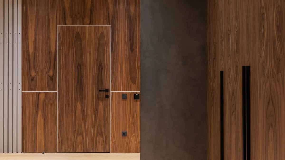 Puerta de madera integrada en una pared revestida del mismo chapado, con tirador negro y sin marco visto.