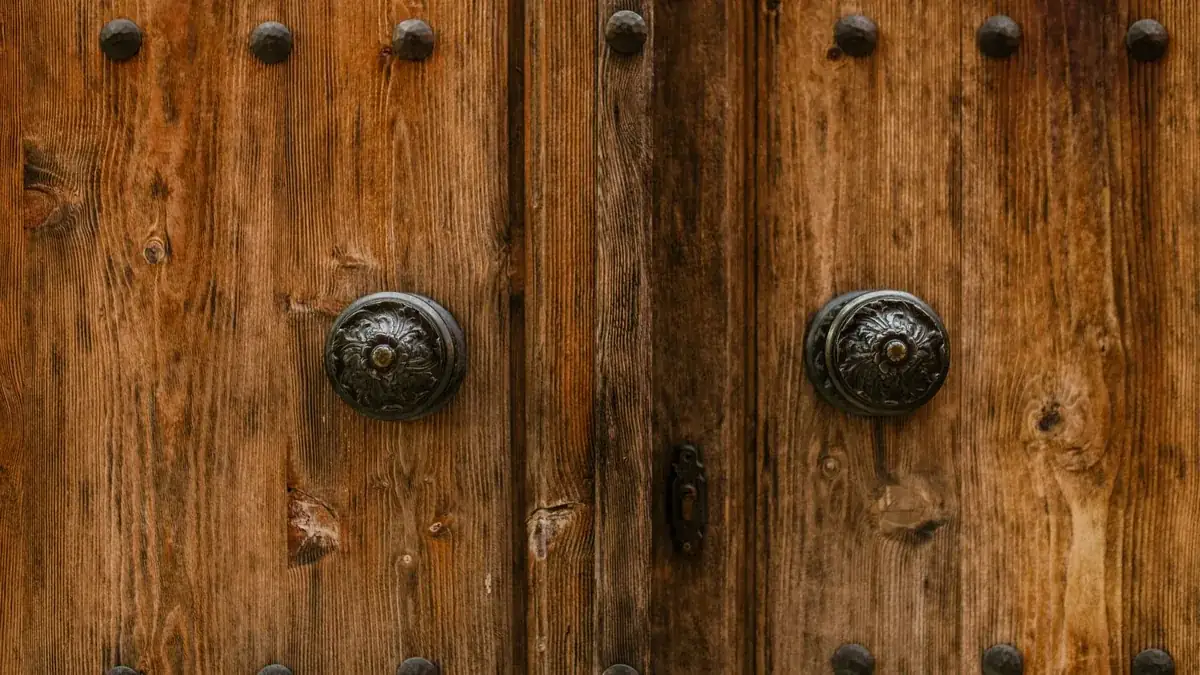 Detalle de una puerta de madera maciza envejecida con dos pomos de hierro y clavos decorativos.