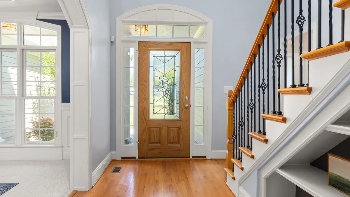 Puerta de entrada de madera con vidrio decorativo y ventanas laterales, junto a una escalera con barandilla de forja.